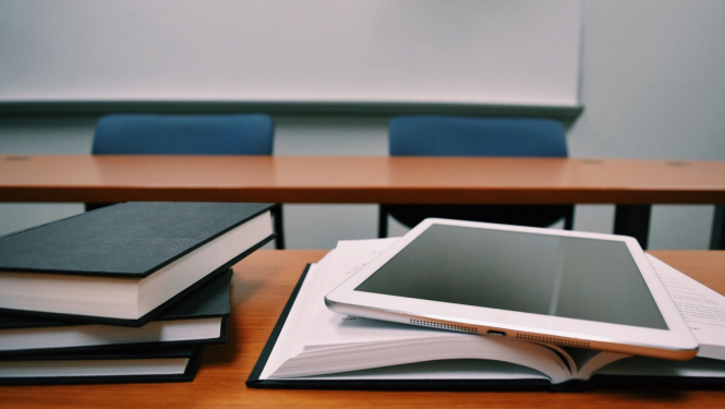 auditorija, uz galda grāmatas un planšete