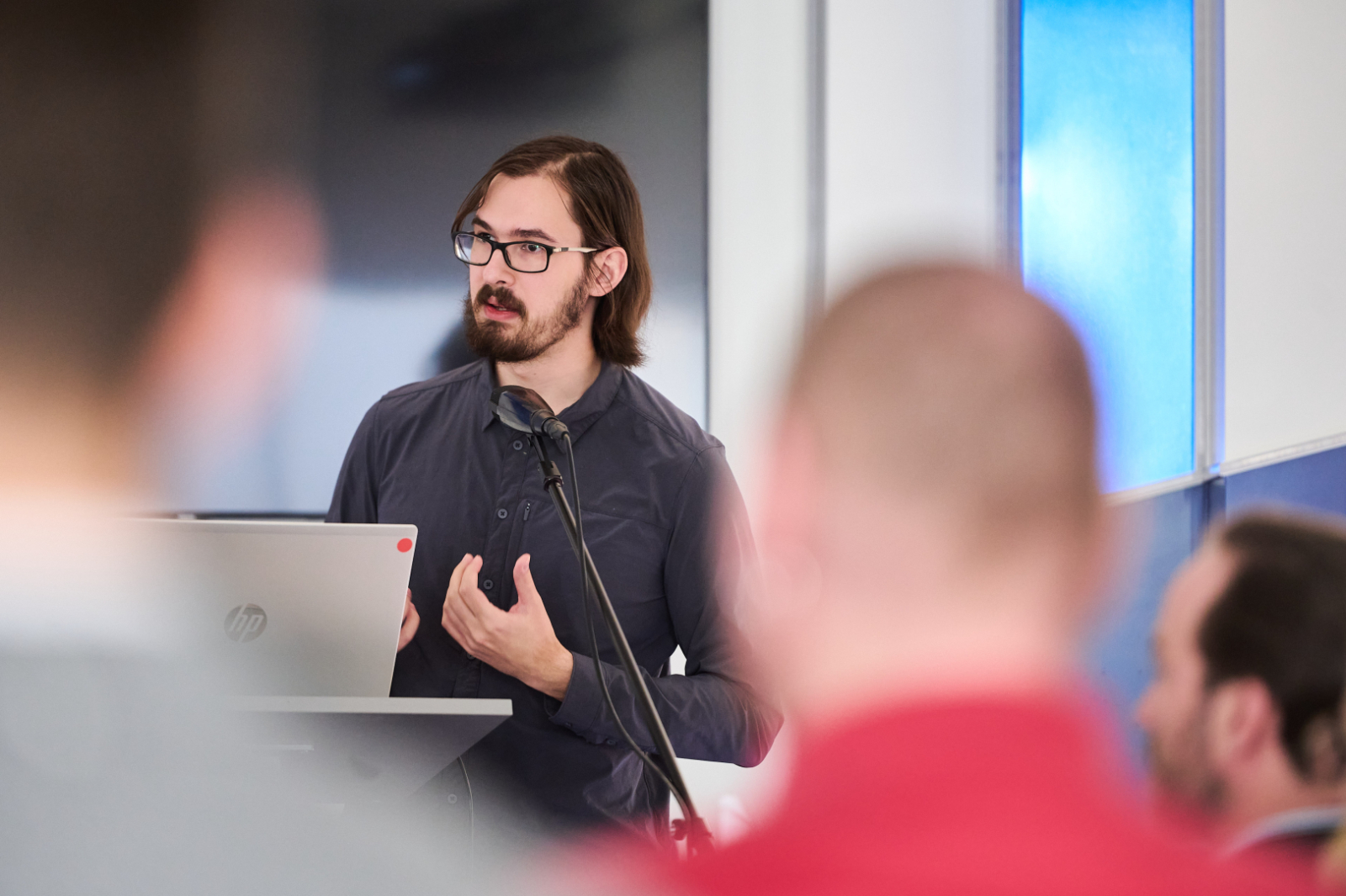 Vīrietis pie mikrofona tumšā kreklā