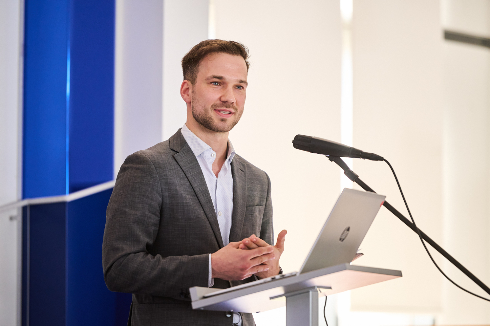 Vīrietis tumšā uzvalkā pie mikrofona